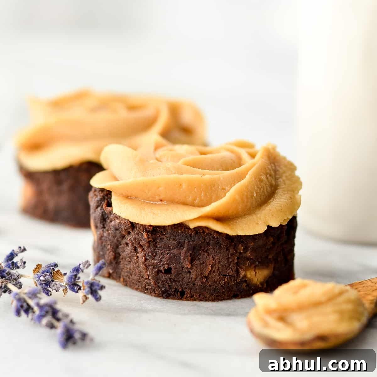 Side view of two brownies frosting with homemade vegan peanut butter frosting piped on in the shape of a rose 