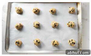 Twelve balls of chocolate chip cookie dough on a sheet pan.