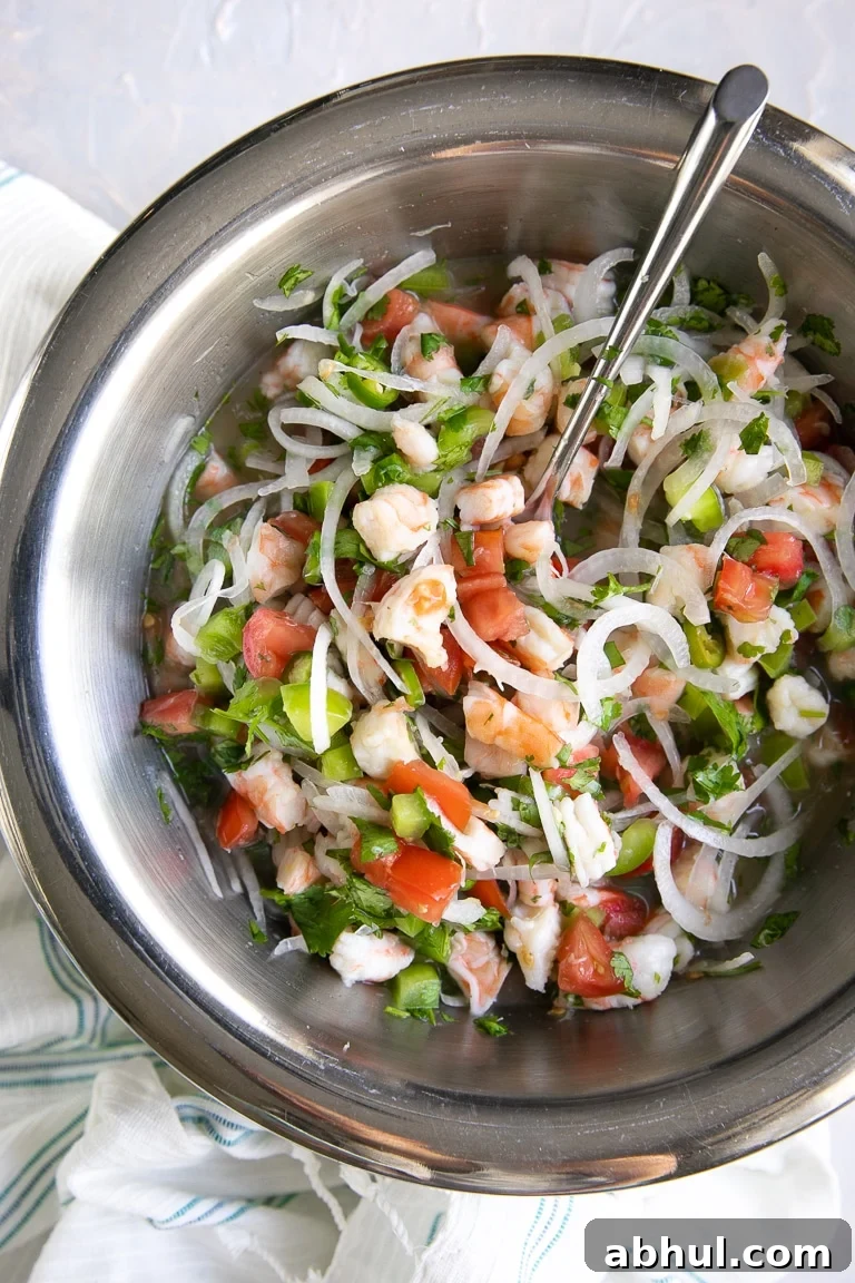 Large mixing bowl filled with shrimp, sliced onion, bell pepper, tomatoes, cilantro, and citrus juice.