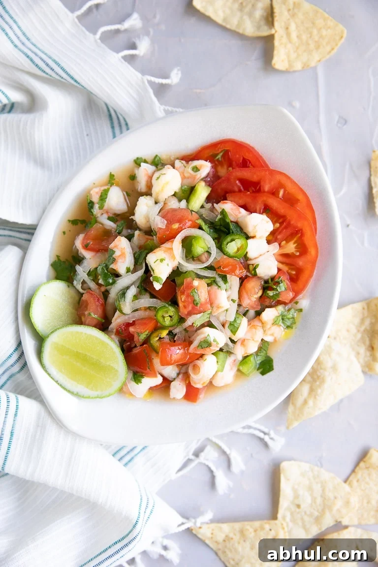 Shrimp Ceviche served in a white bowl and garnished with fresh sliced tomatoes, lime, and tortilla chips.