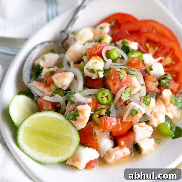 White shallow serving plate filled with shrimp ceviche made with chopped shrimp, sliced onion, chopped bell peppers, and tomatoes in citrus juice with chopped cilantro and chopped jalapenos.