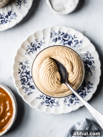 A thin glass cup holds circular swirls of piped dulce de leche mousse with a spoon resting in it.