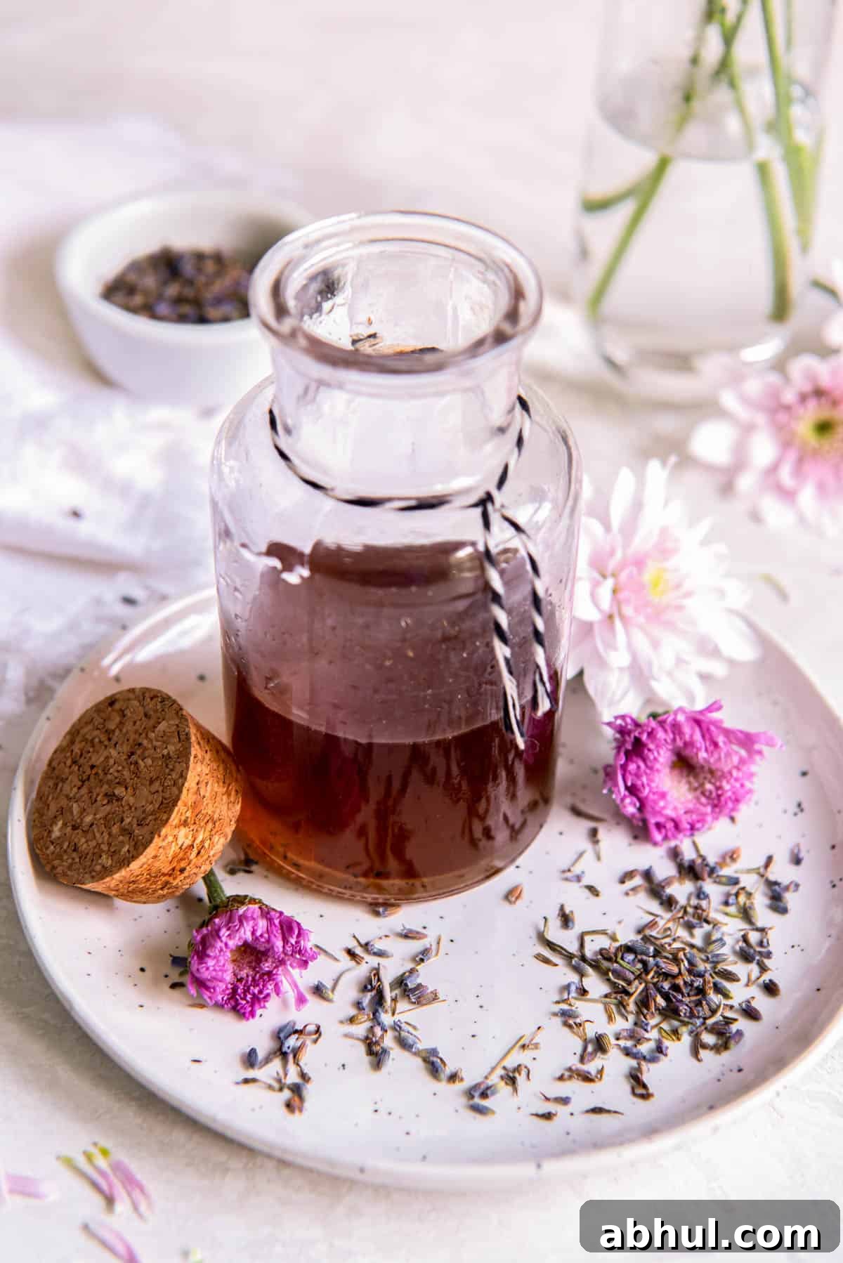 Vanilla lavender simple syrup in a glass jar sitting on a small plate with fresh lavender buds sitting to the side. 