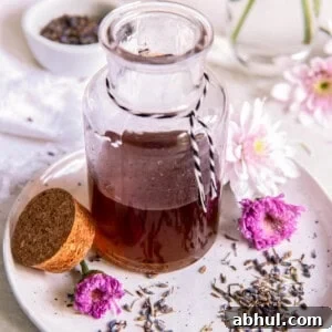 Vanilla lavender simple syrup in a glass jar sitting on a small plate with fresh lavender buds sitting to the side.
