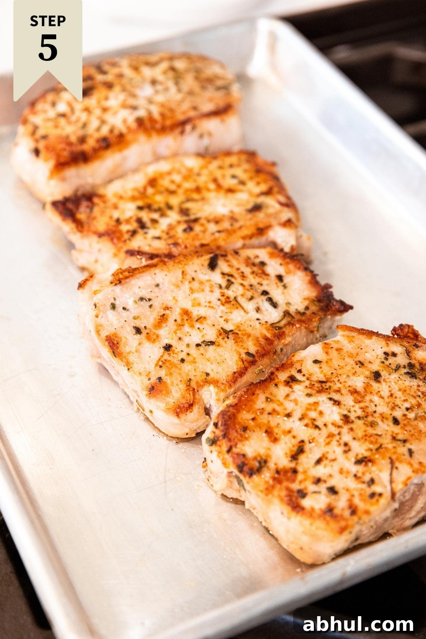 Browned and fully cooked pork chops sitting on metal baking dish on stovetop after being removed from skillet.