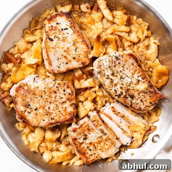 Large metal skillet sitting on white marble with cooked pork chops and mashed apples underneath right after coming out of the oven.