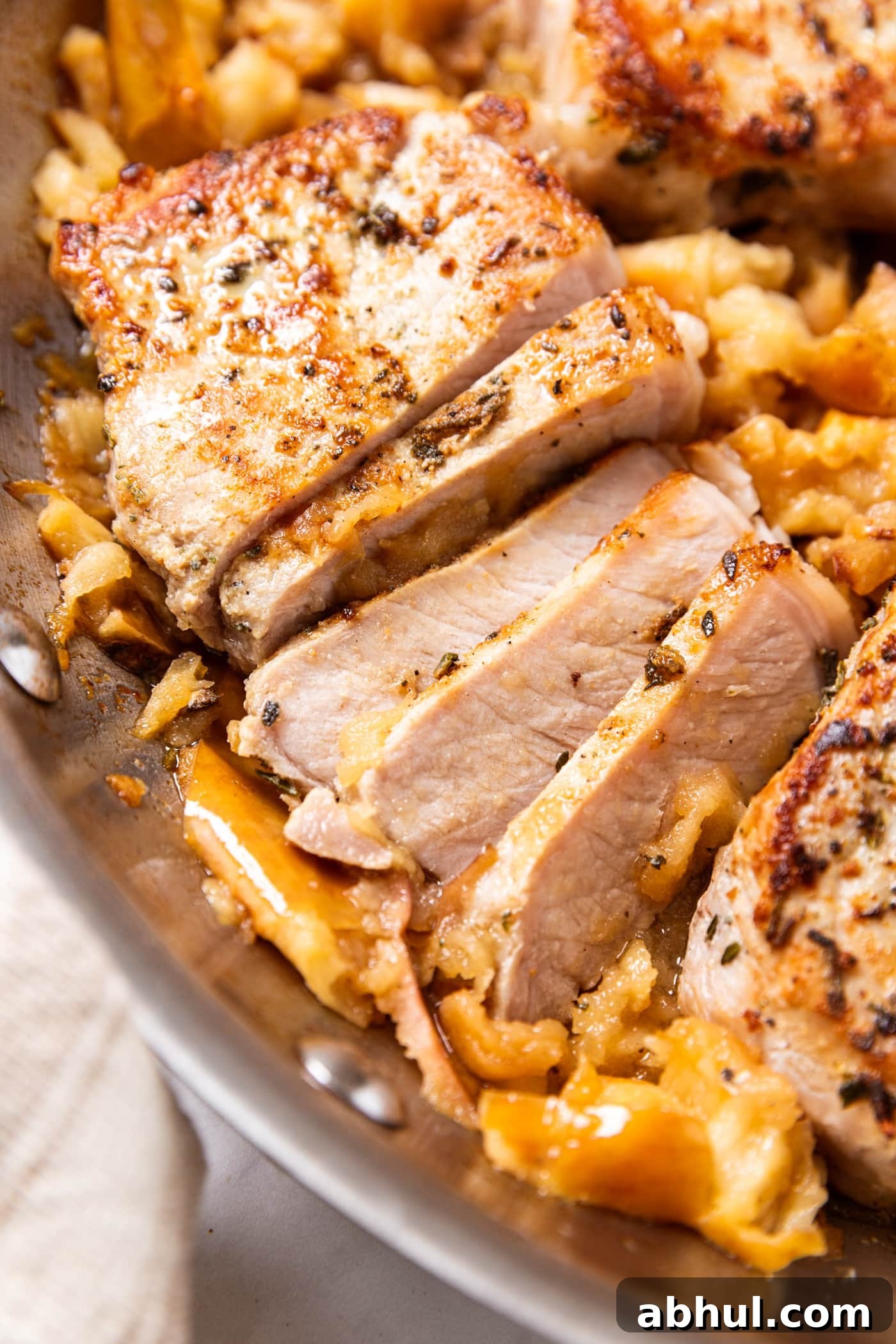Metal skillet filled with smashed apples and browned pork chops with part of one sliced into slices.