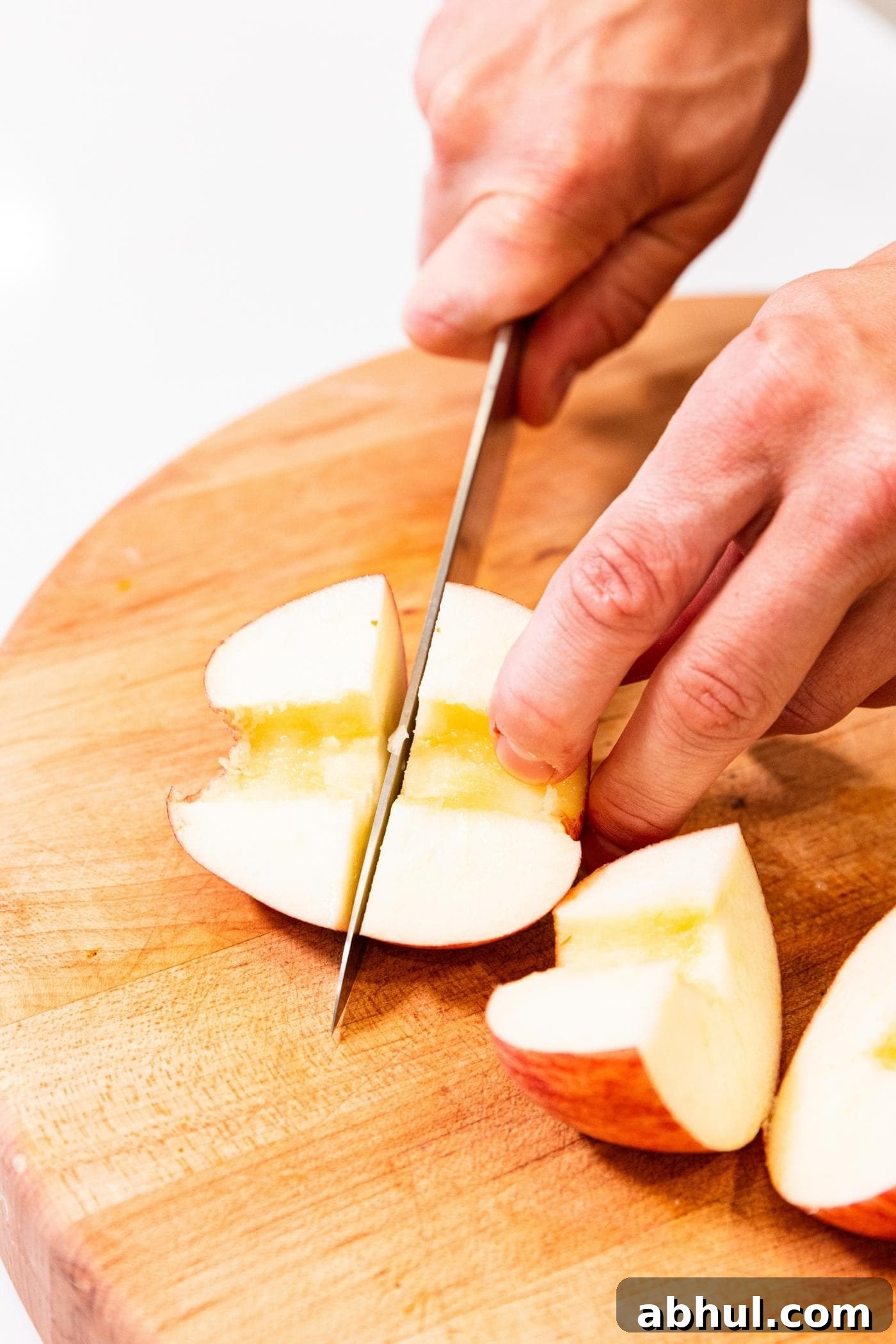 Two hands slicing up apples on wood cutting board.