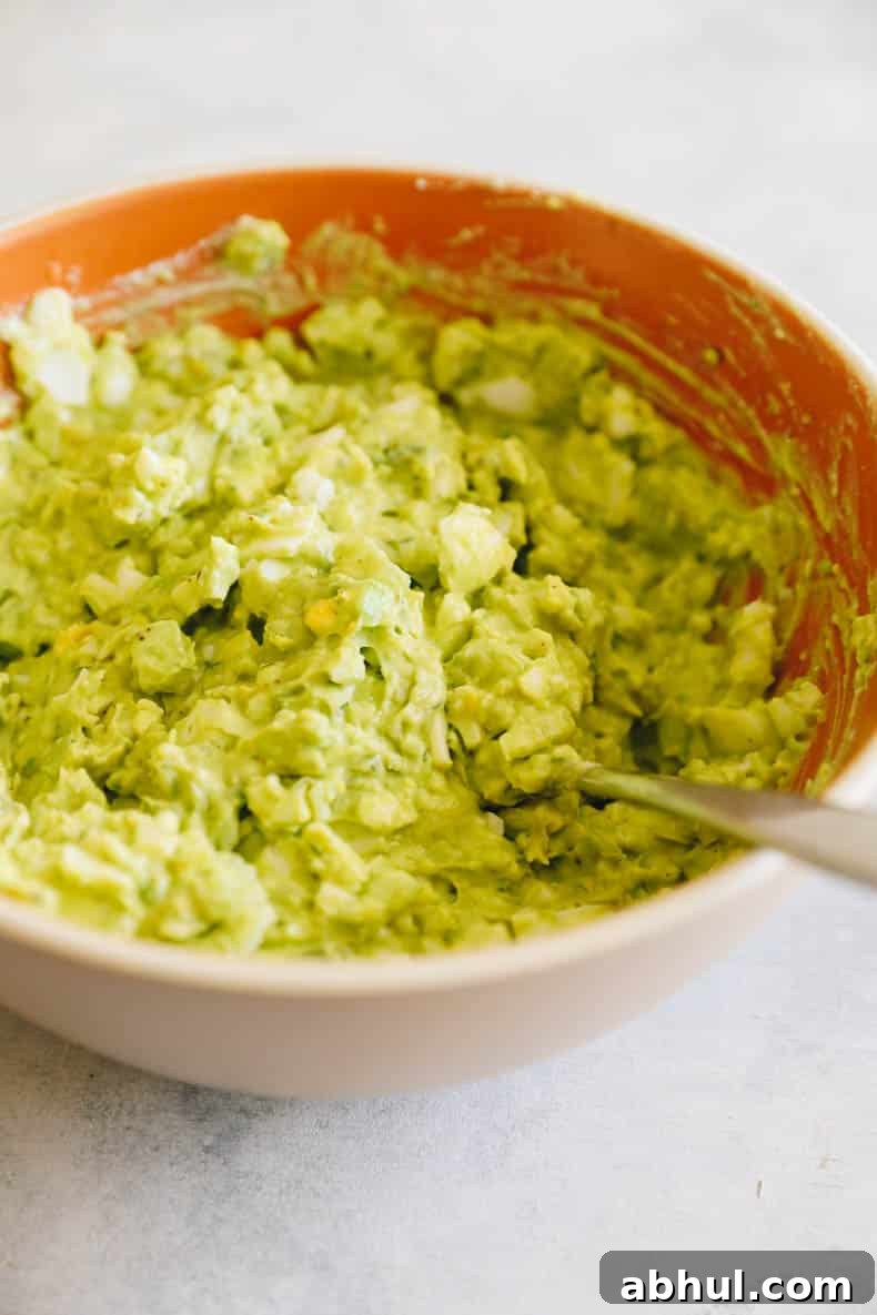 avocado egg salad in a large brown bowl with a spoon.