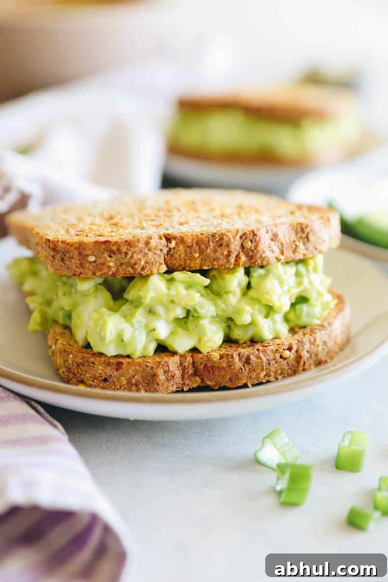 avocado egg salad between two slices of bread on a white plate.