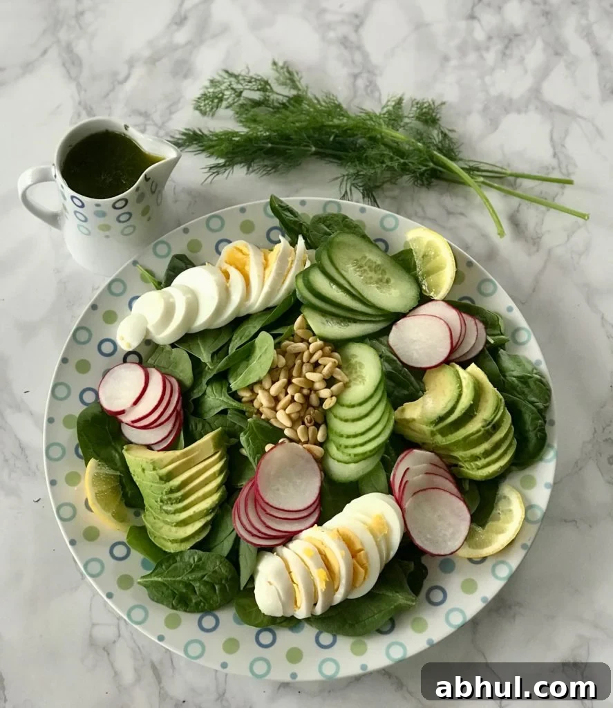 Sliced boiled eggs, avocado, cucumbers, and pine nuts on a bed of spinach 