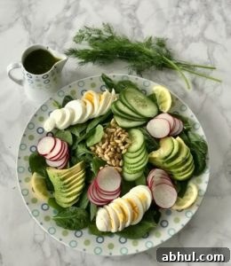 Sliced boiled eggs, avocado, cucumbers, and pine nuts on a bed of spinach