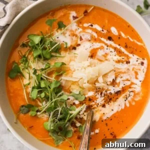 a closeup of creamy butternut squash soup with coconut milk topped with parmesan cheese, microgreens, and black pepper