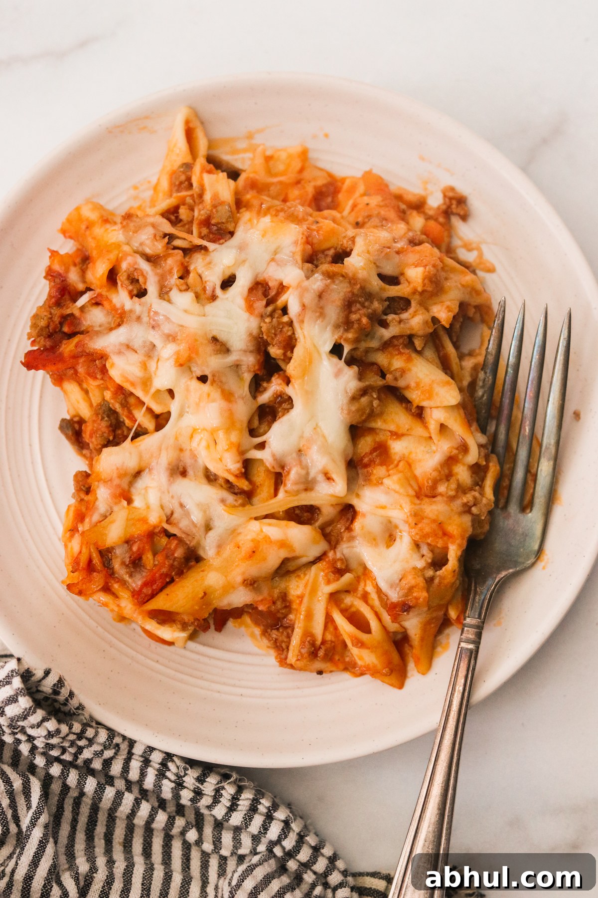 Plate with a serving of hidden veggie lasagna and a fork placed on a white countertop.