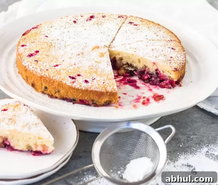 sliced Nantucket cranberry cake on a cake stand with a sifter of powdered sugar in front of it