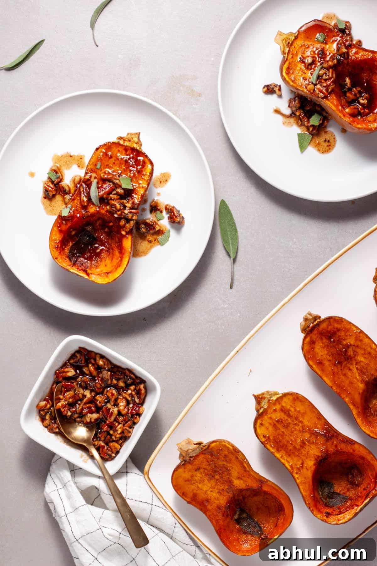 Maple-Pecan Roasted Honeynut Squash Recipe 2 Roasted honeynut squash topped with candied pecans and sage on a white plate with a platter of more off center.