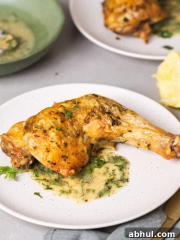 A serving of golden brown roasted chicken leg quarters with an herb sauce on a gray table.