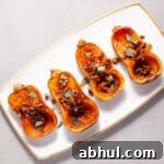 Roasted honeynut squash with maple pecans on a serving platter topped with fresh sage.