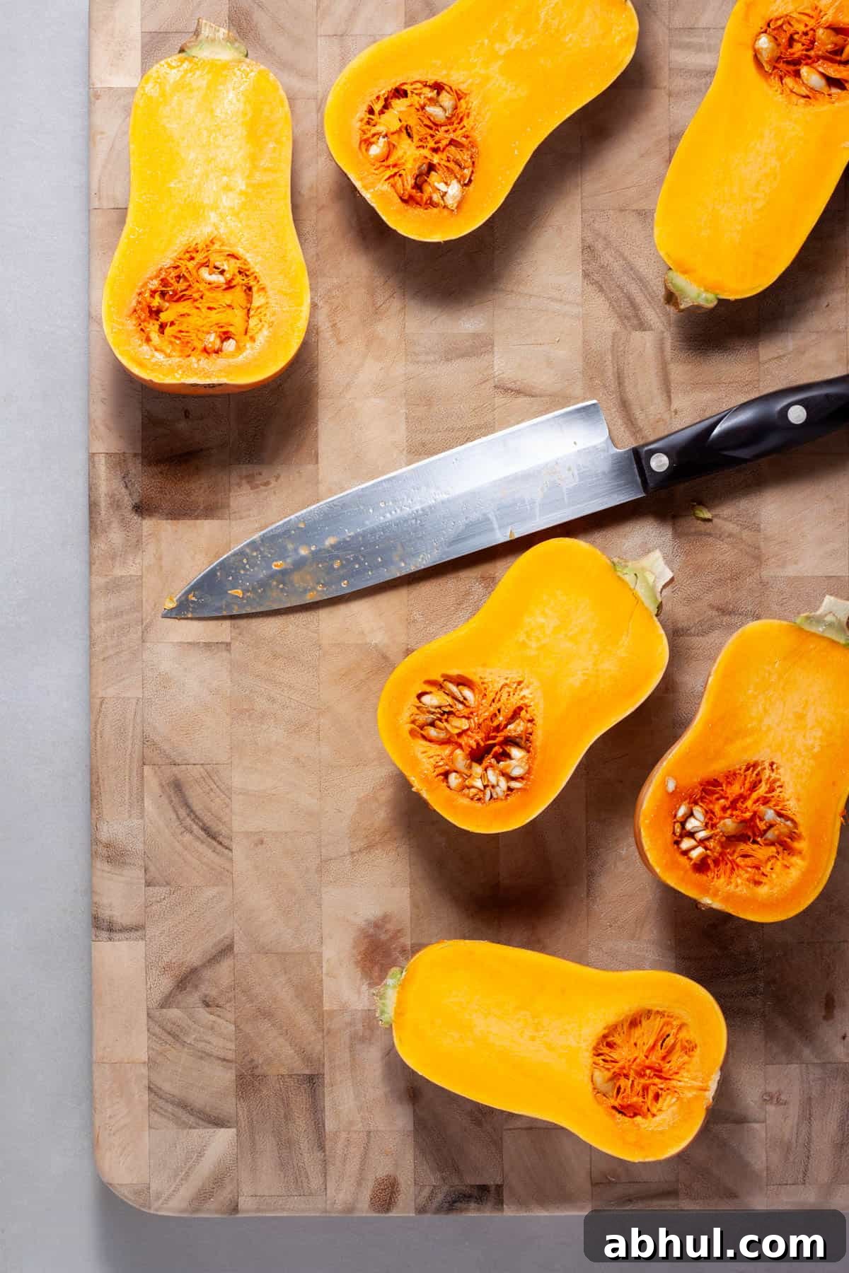 Maple-Pecan Roasted Honeynut Squash Recipe 4 Honeynut squash getting cut in half on a wooden cutting board.