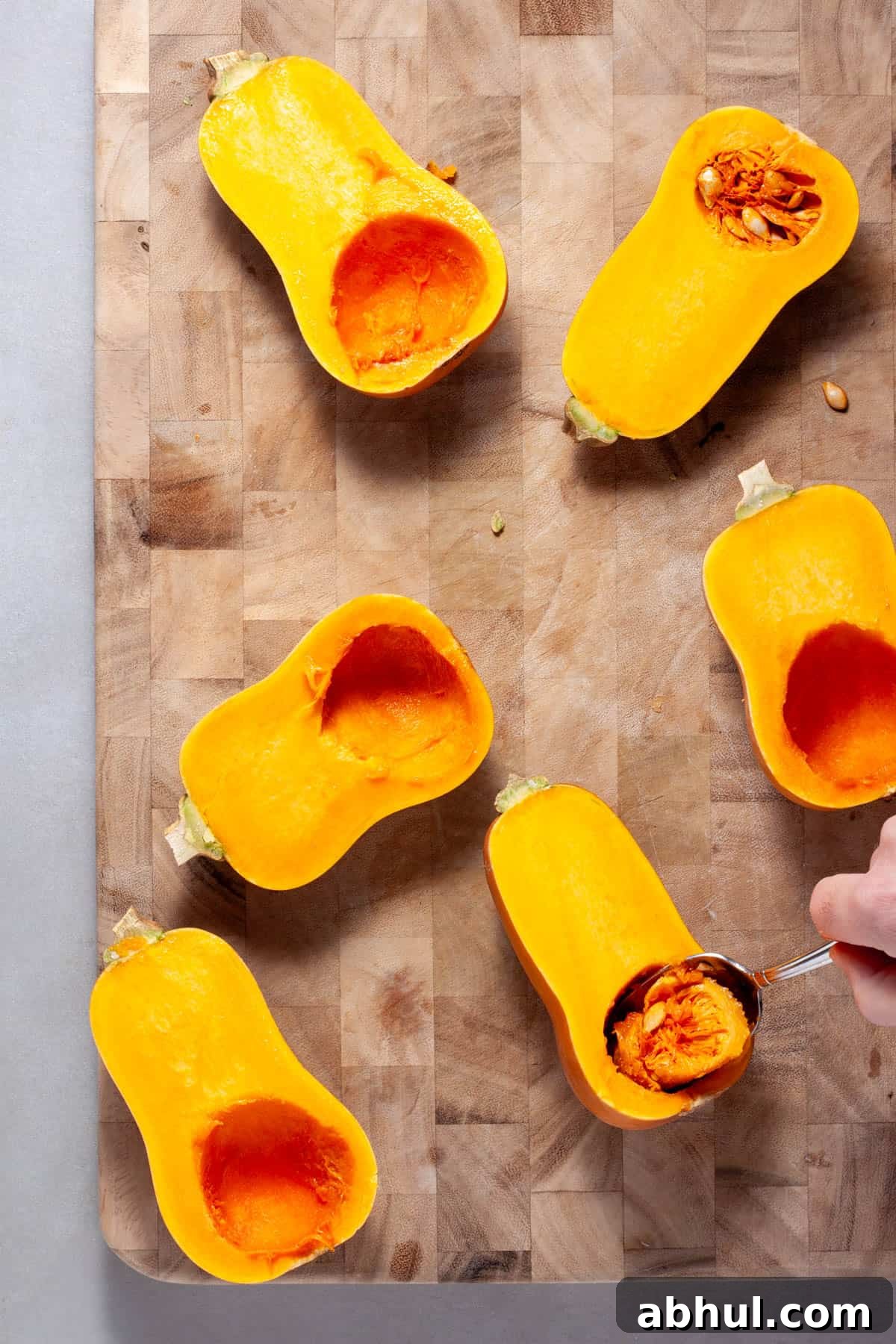 Maple-Pecan Roasted Honeynut Squash Recipe 5 The inside of honeynut squash getting scooped out with a spoon on a wooden cutting board.