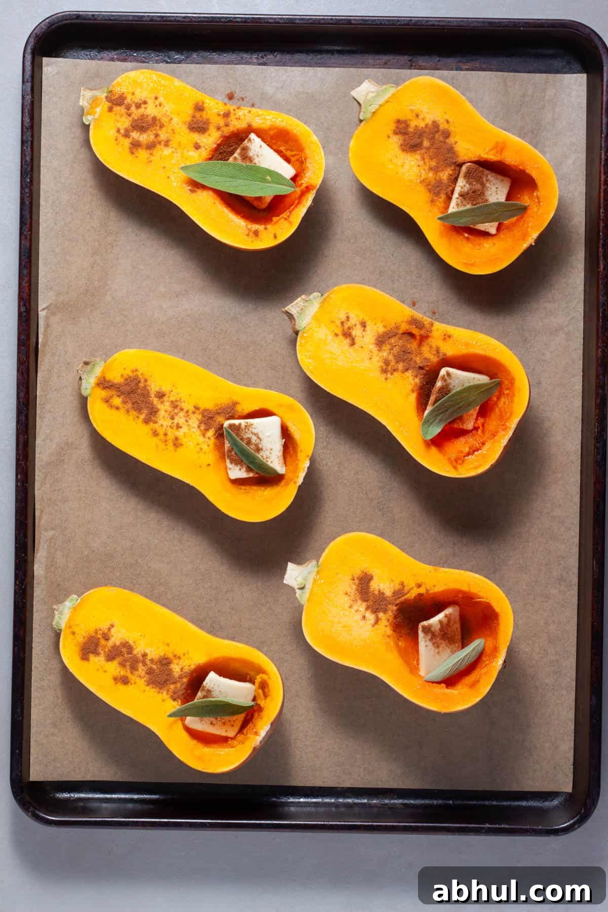 Maple-Pecan Roasted Honeynut Squash Recipe 6 Halved honeynut squash on a parchment lined baking sheet with butter, cinnamon and sage in each cavity.