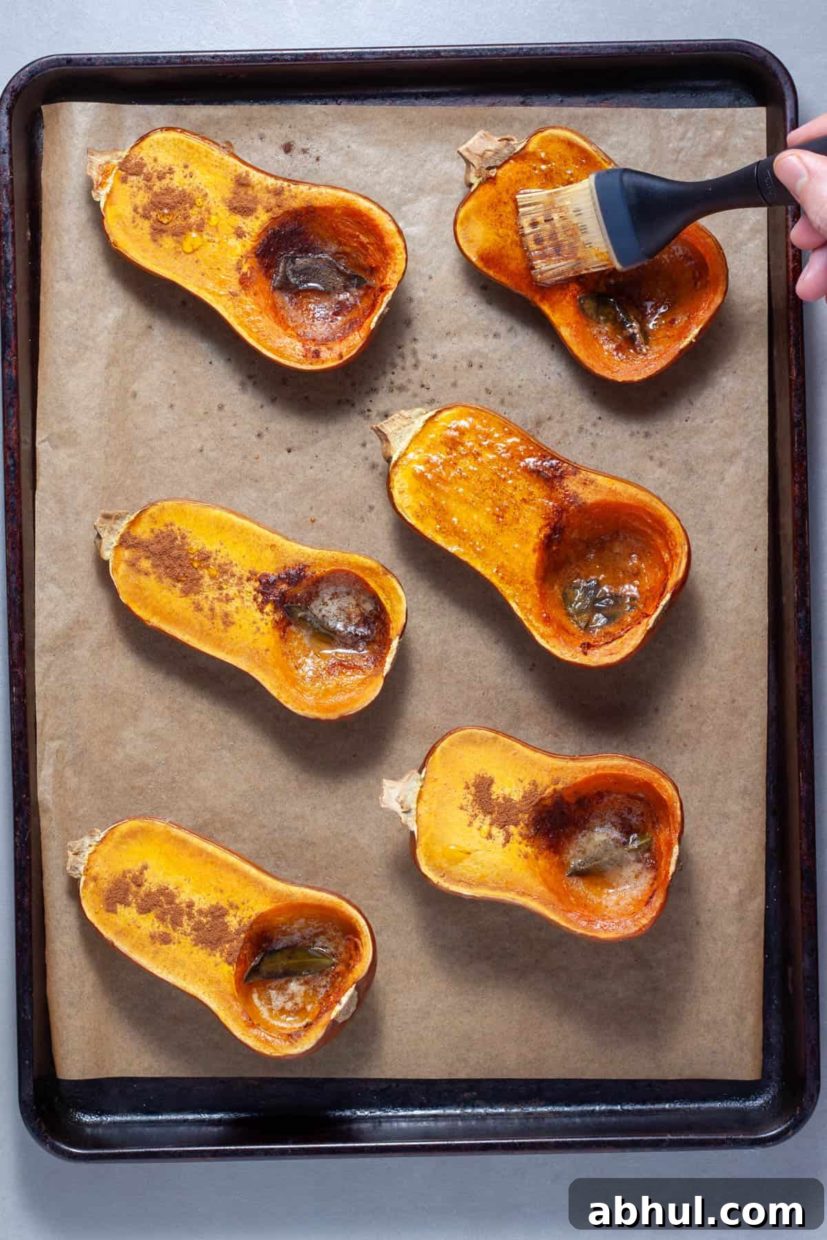Maple-Pecan Roasted Honeynut Squash Recipe 8 Roasted honeynut squash on a baking sheet getting brushed with melted butter and sage.