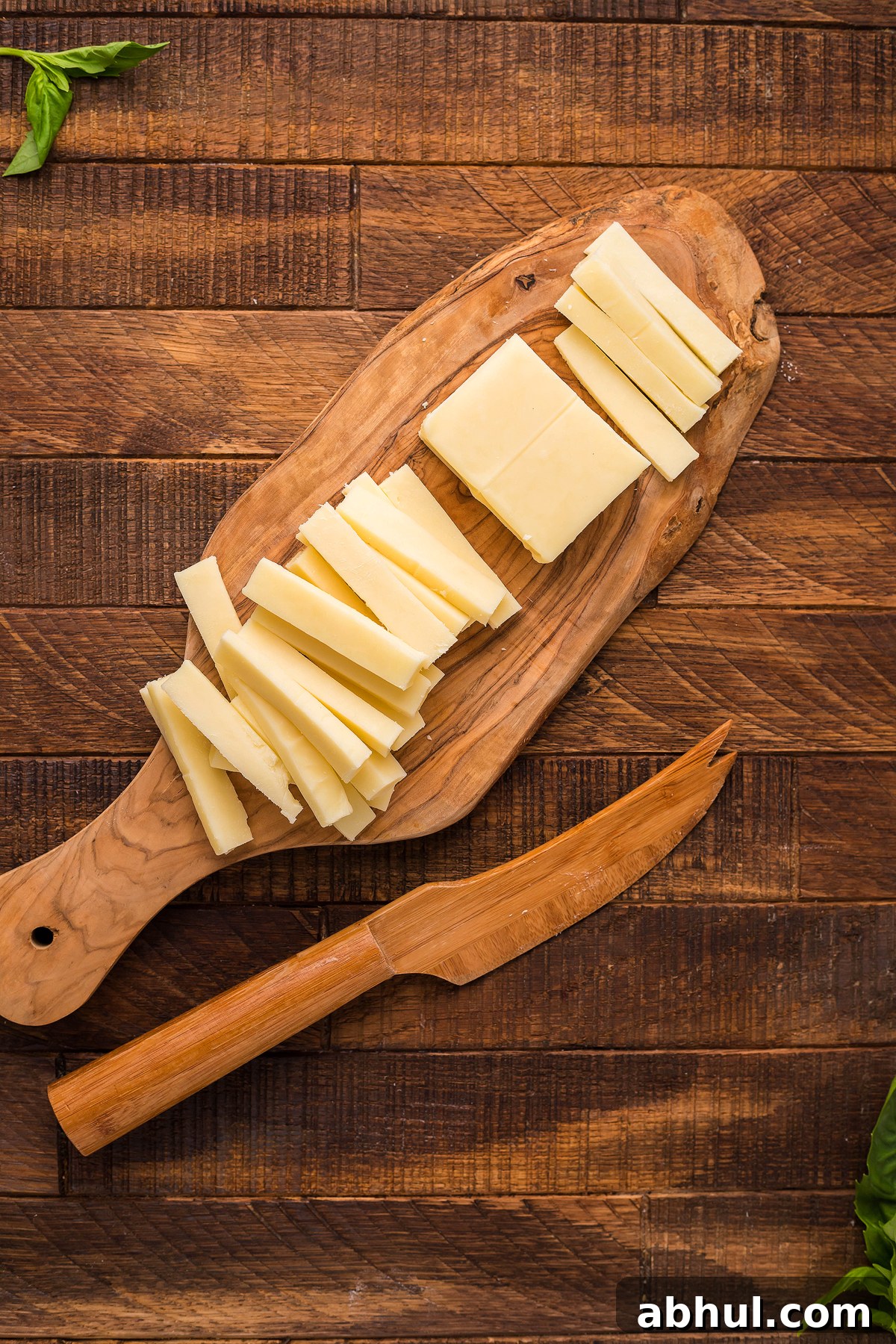 Sliced white cheese on a wooden board with a wooden knife.