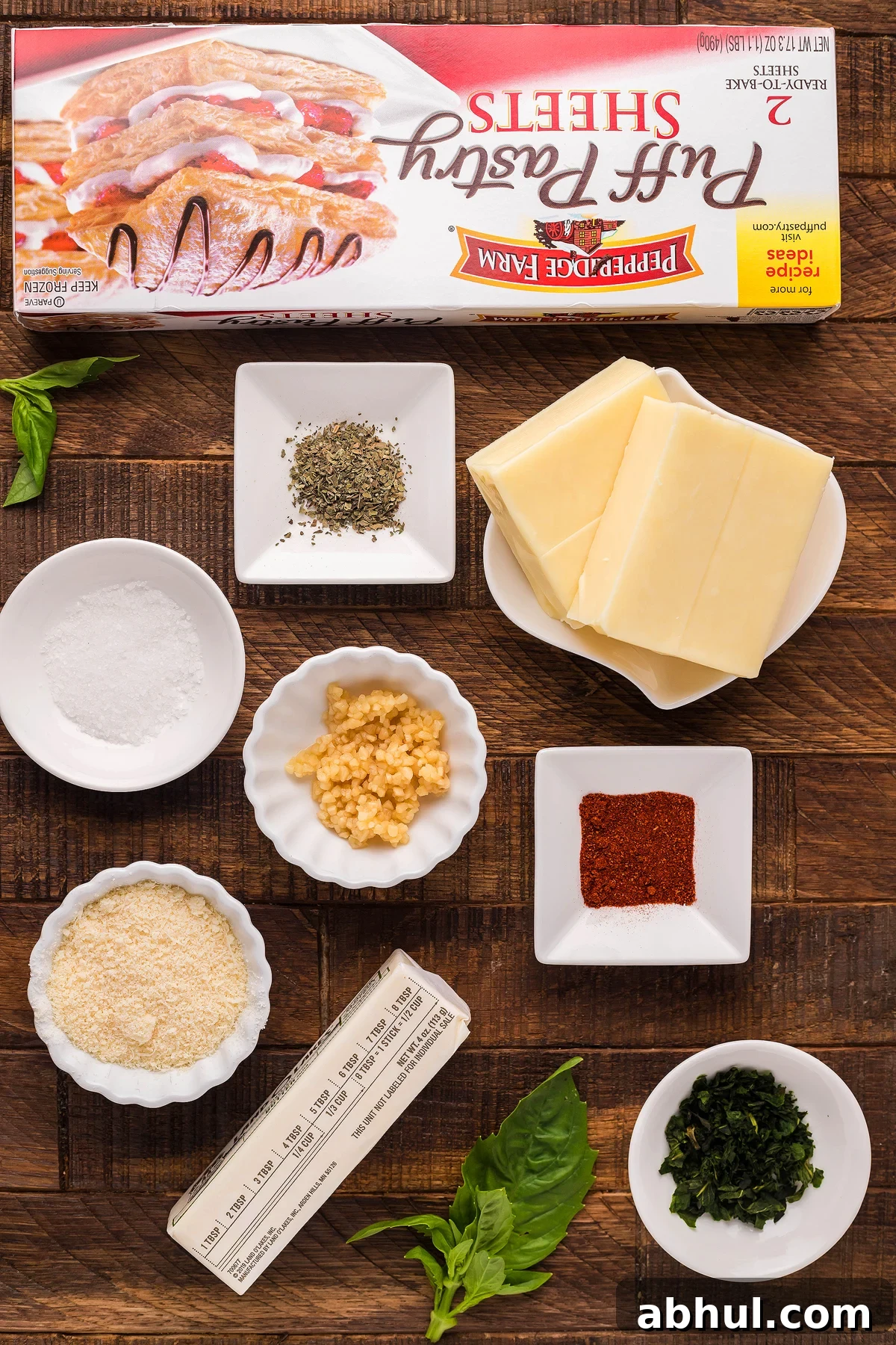 Ingredients for a recipe are elegantly arranged on a wooden surface, showcasing everything needed for puff pastry cheese straws from scratch.
