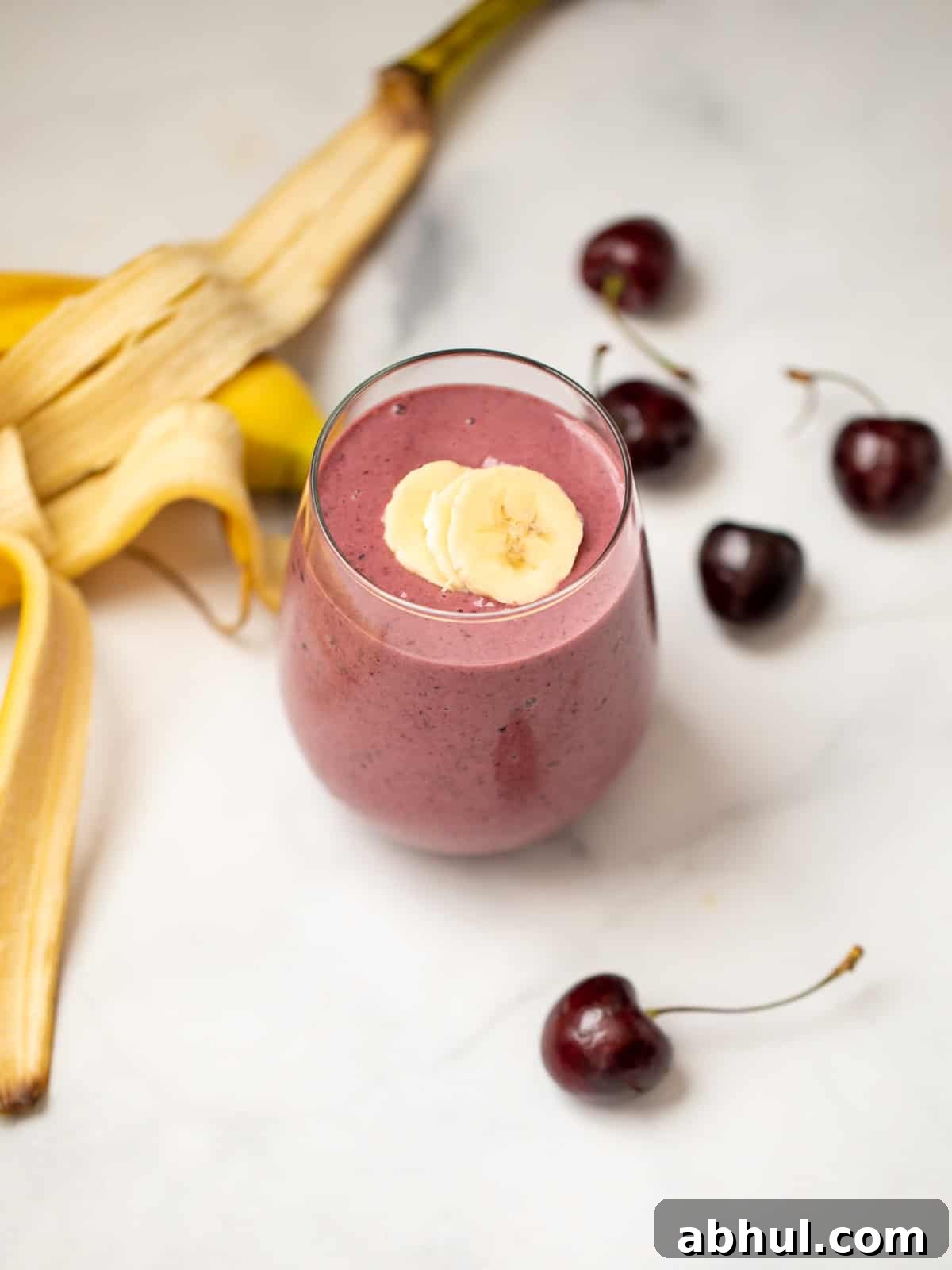 Cherry Smoothie in clear glass next to fresh cherries and banana.