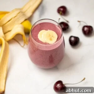 Cherry Smoothie in clear glass with sliced bananas on top and fresh cherries in background.
