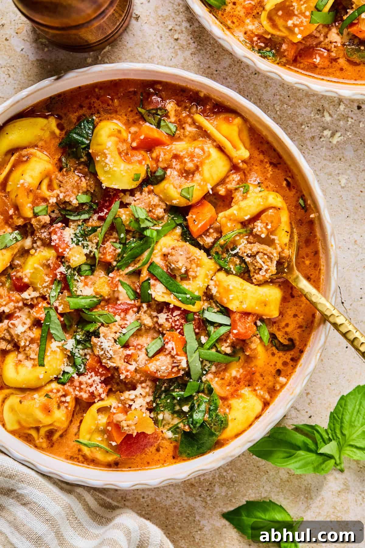 Bowl with sausage tortellini soup topped with fresh basil.