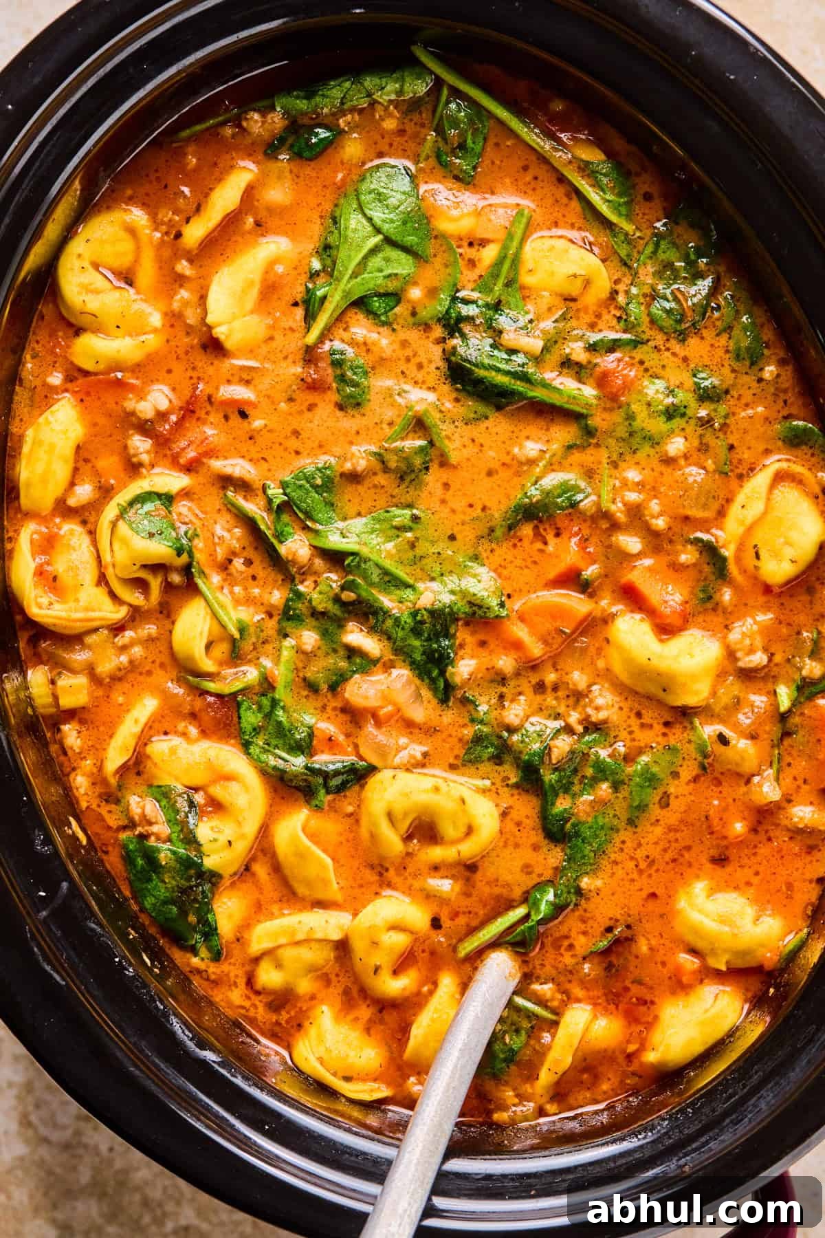 Sausage tortellini soup in slow cooker with ladle.