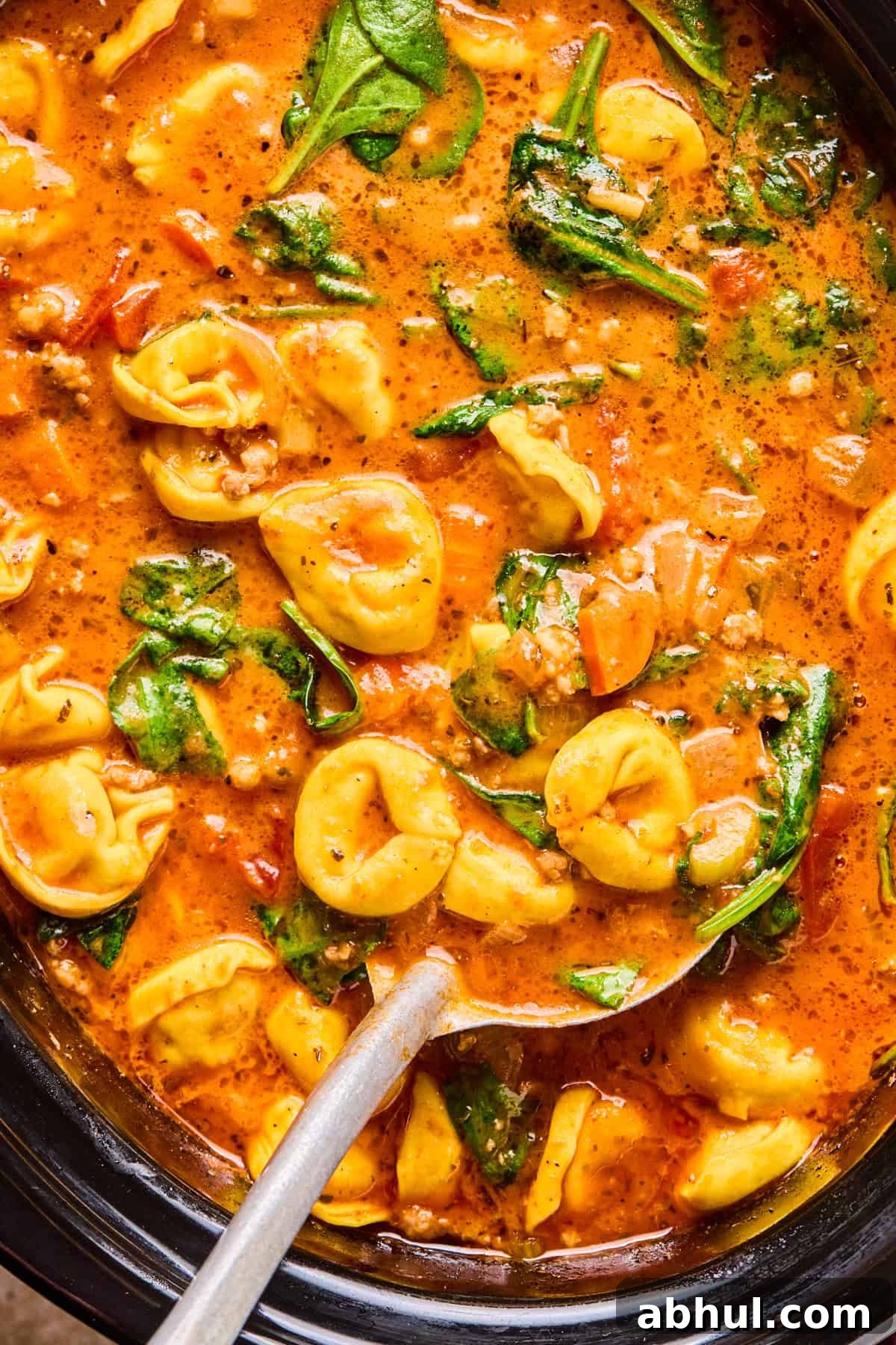 Crockpot with tomato based soup with sausage and tortellini and ladle spooning soup.