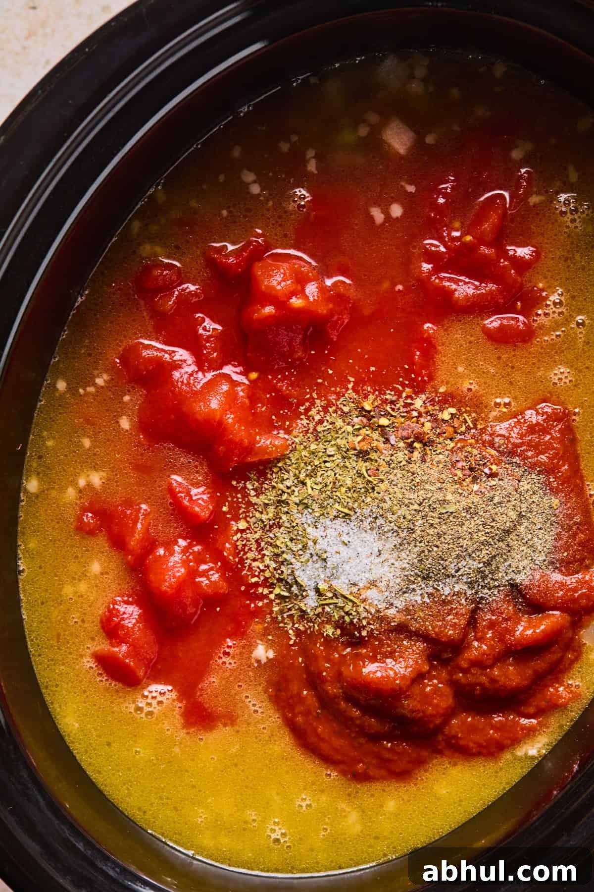 Broth, marinara, tomatoes, and spices added to slow cooker with meat and vegetables.