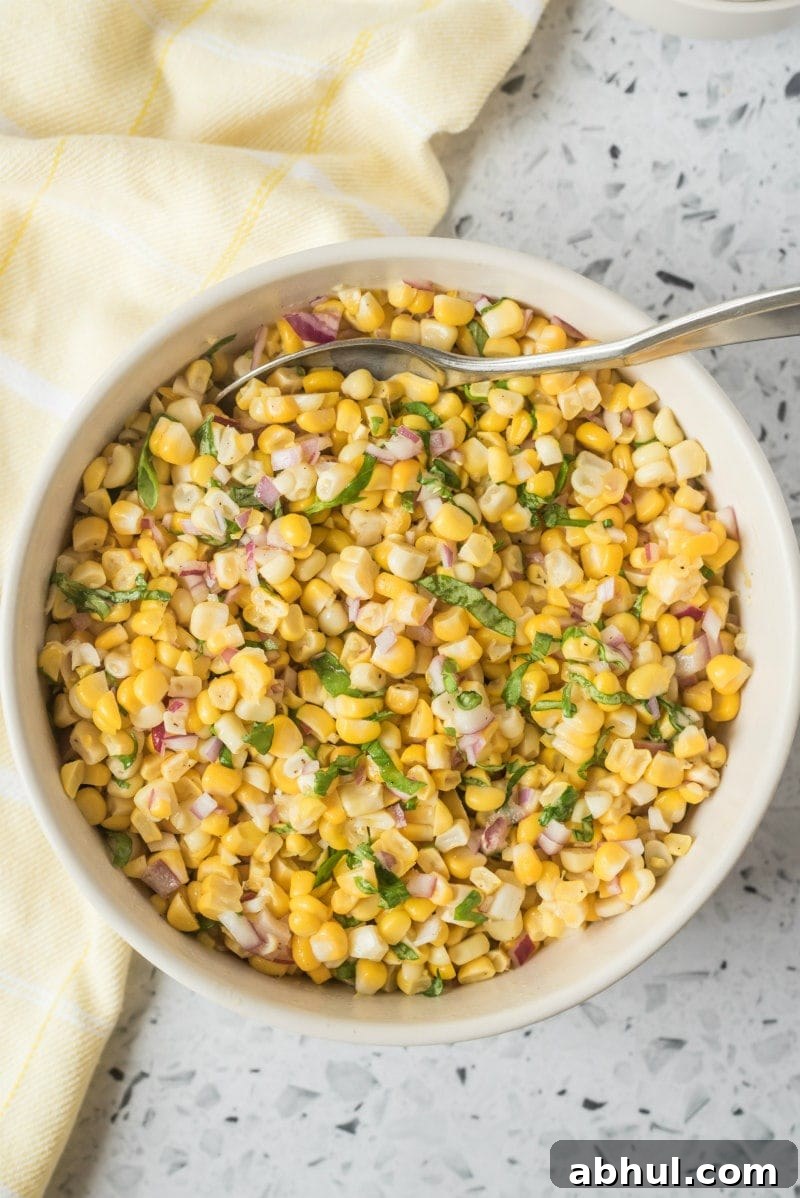Fresh Corn Salad overhead shot of fresh corn salad in a white bowl with a serving spoon. light yellow napkin displayed on the side
