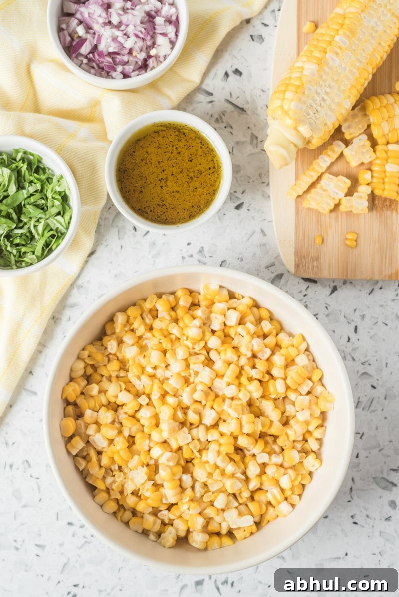 Fresh Corn Salad ingredients overhead shot of fresh corn salad ingredients: fresh corn, basil, red onion and dressing all displayed in white bowls