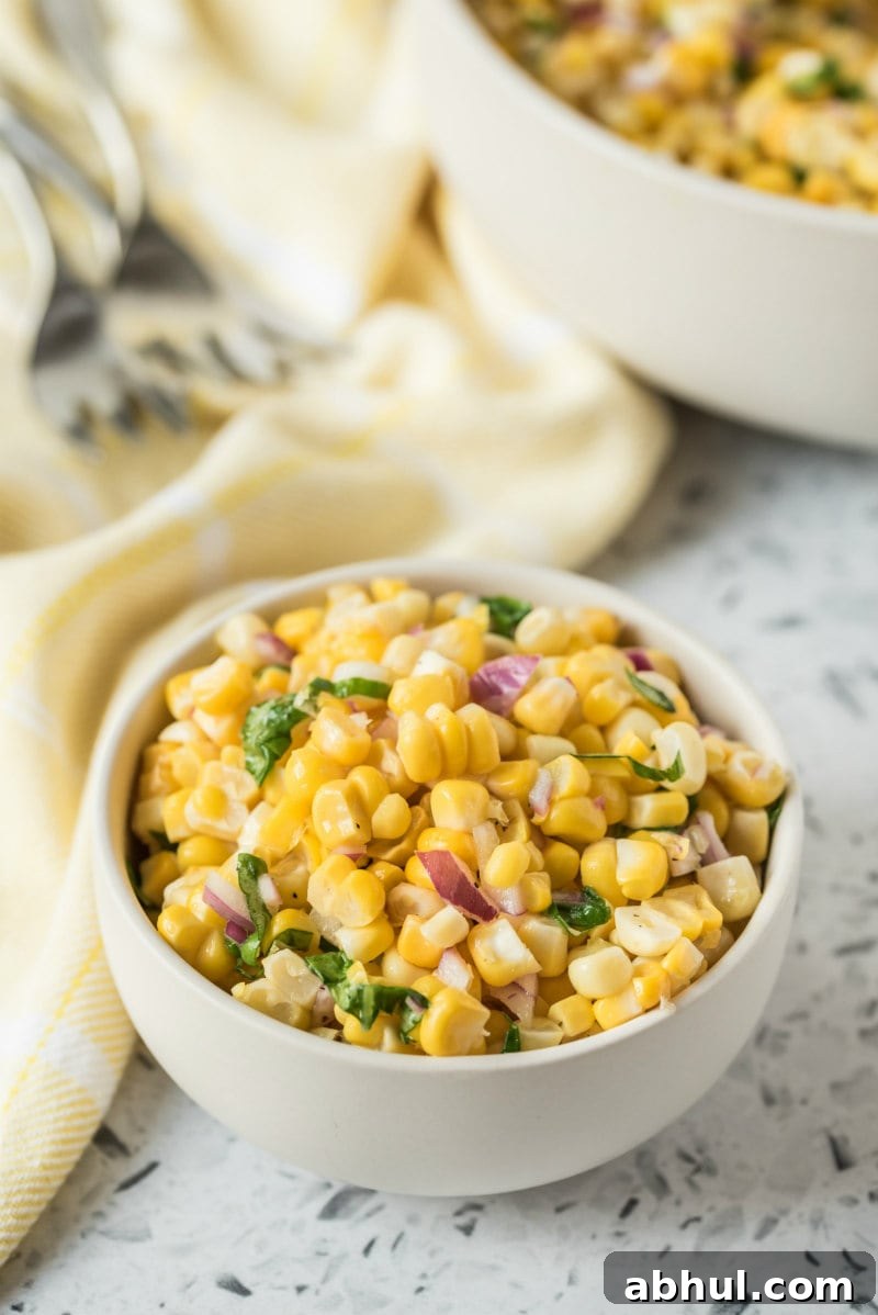 Serving of fresh corn salad serving of fresh corn salad in a white bowl. larger bowl of corn salad in the background. forks and light yellow napkin displayed too.