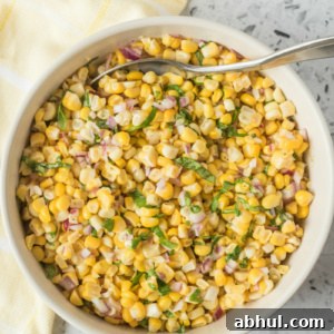 Crisp Summer Corn Salad with Cherry Tomatoes and Basil 2 overhead shot of fresh corn salad in a white bowl with a serving spoon. light yellow napkin displayed on the side