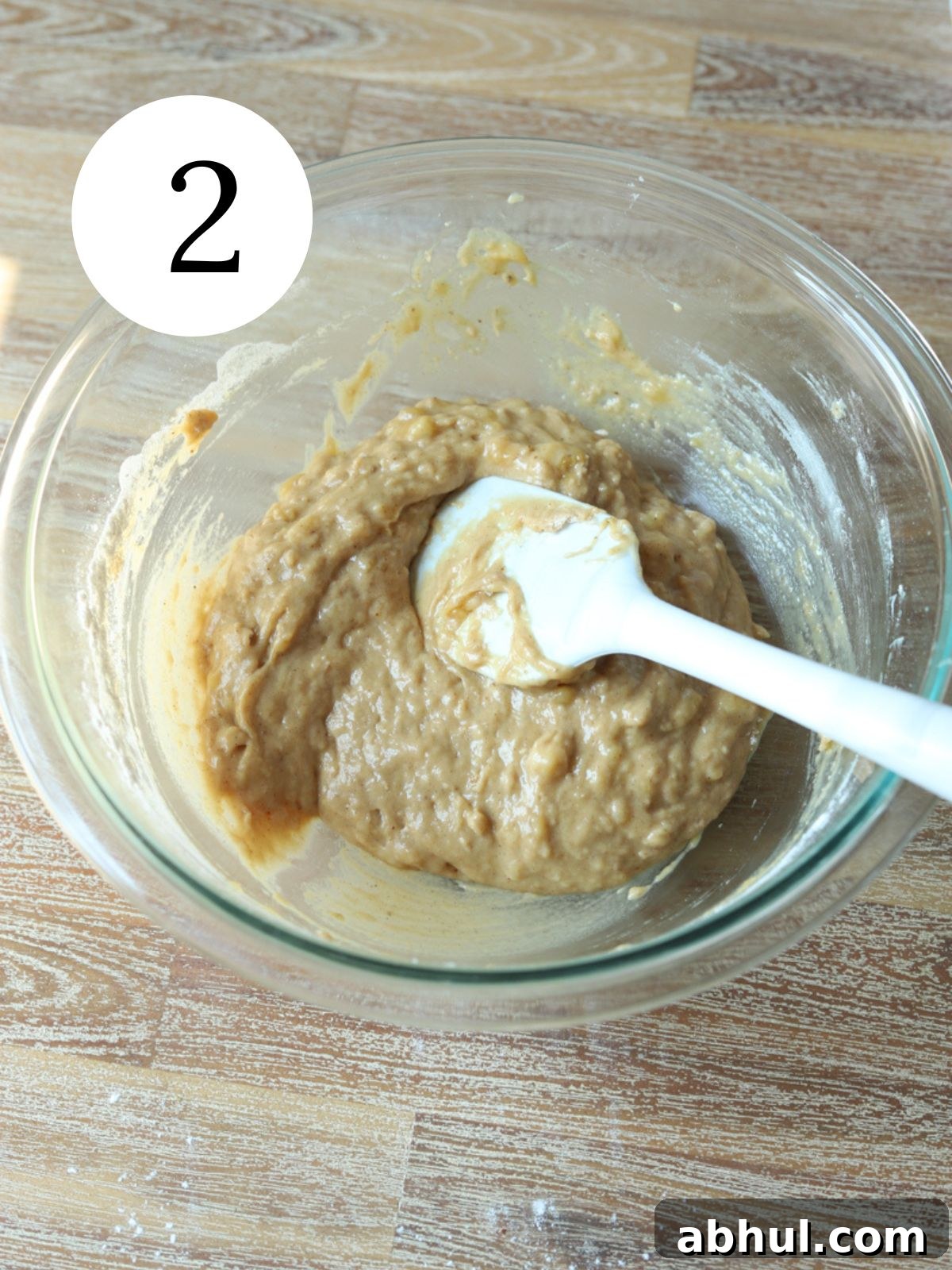 A glass bowl with brown batter and a spatula in it.