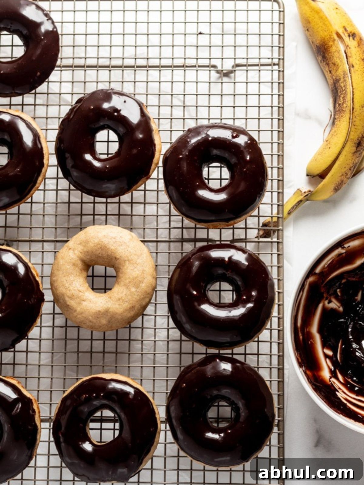 Donuts topped with chocolate ganache on a rack next to a banana.