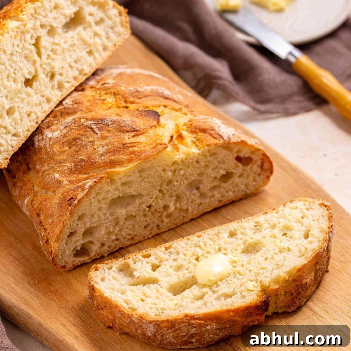 Sliced Italian artisan bread with buttered slice in front.