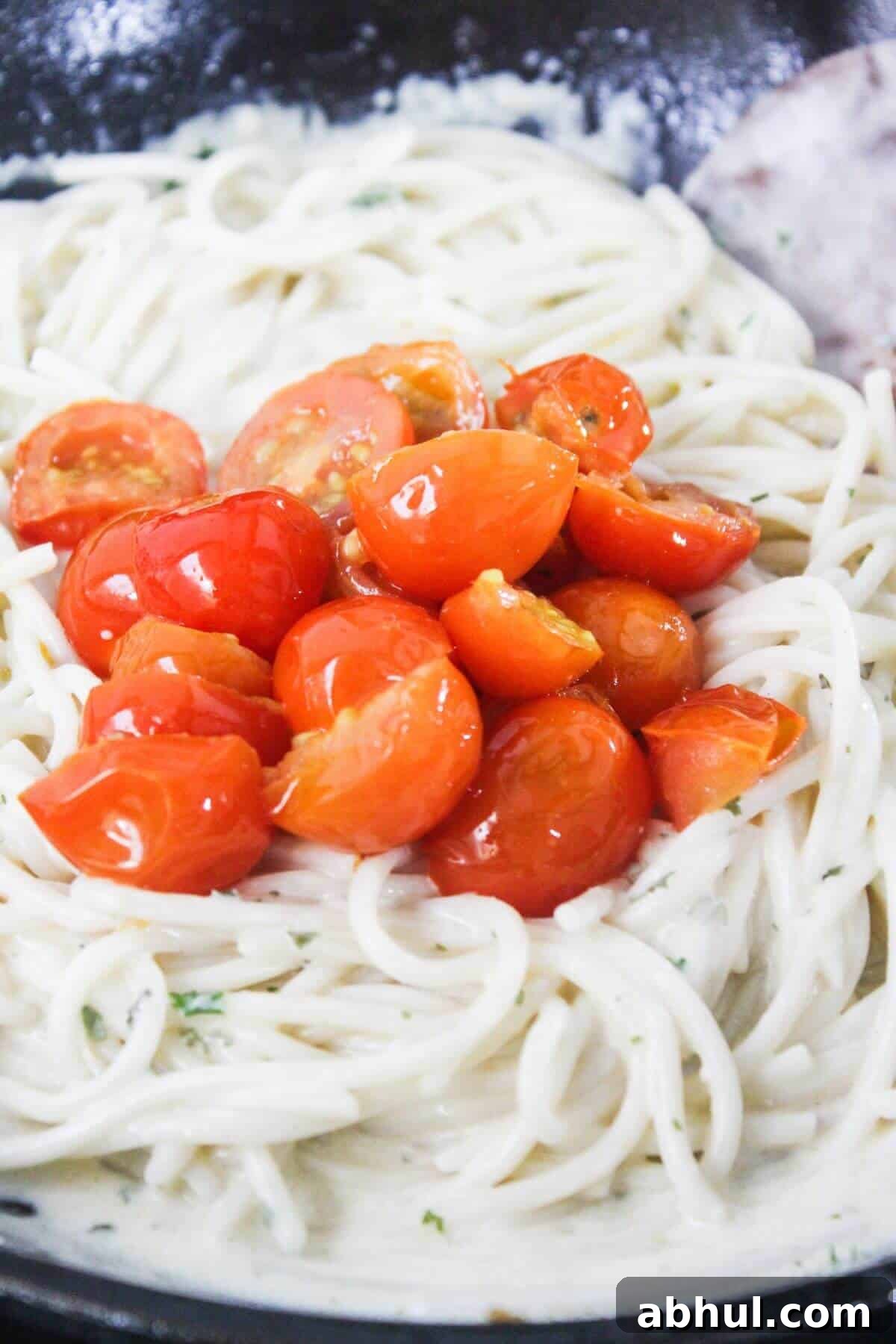 Spaghetti in a creamy white sauce topped with halved cooked cherry tomatoes.