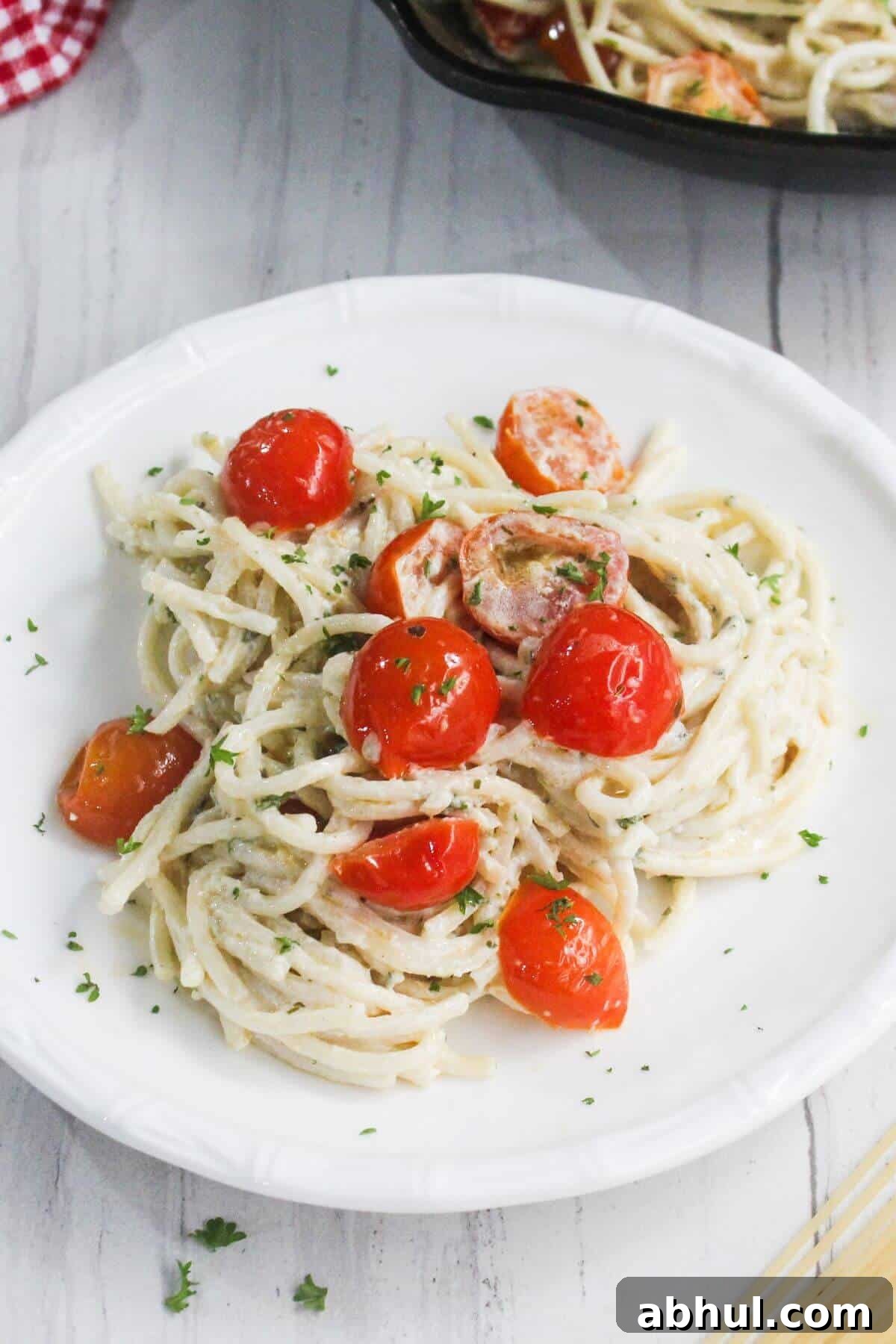 A plate of spaghetti with a creamy white sauce, cherry tomatoes, and chopped herbs, served on a white dish.