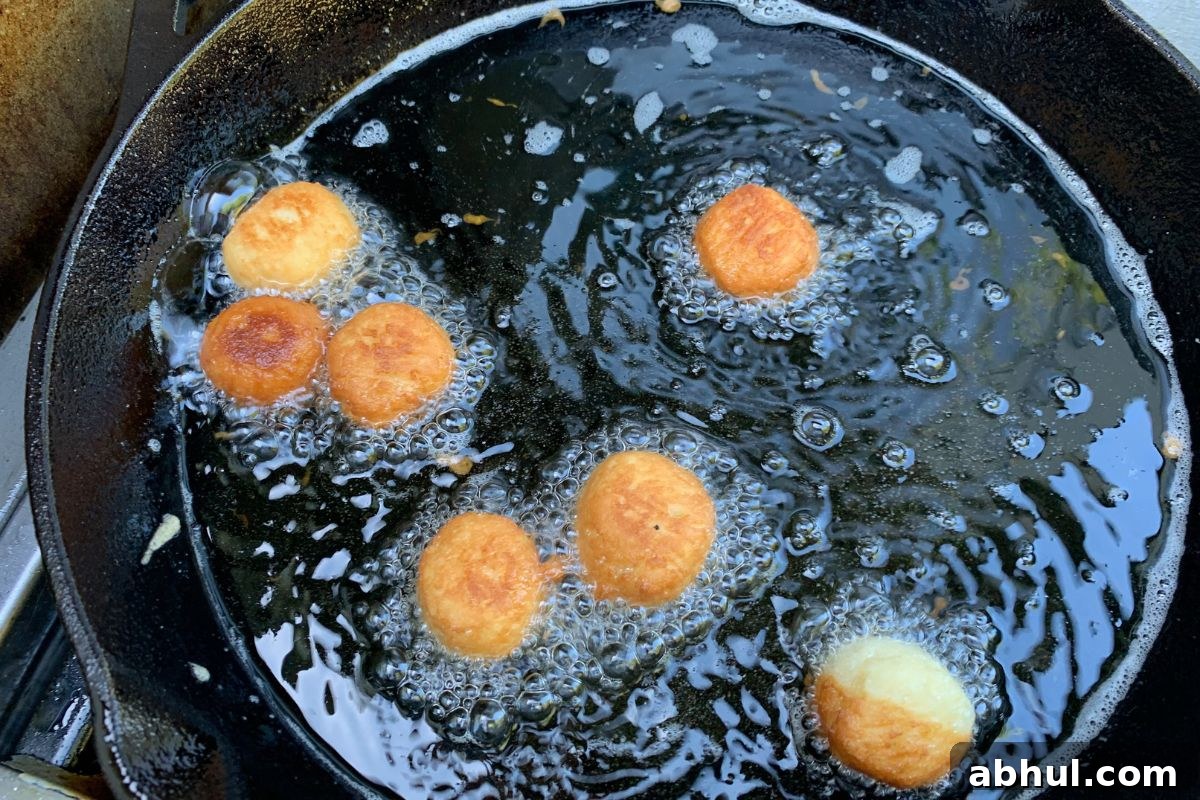 Donut holes frying in oil in a cast iron skillet.