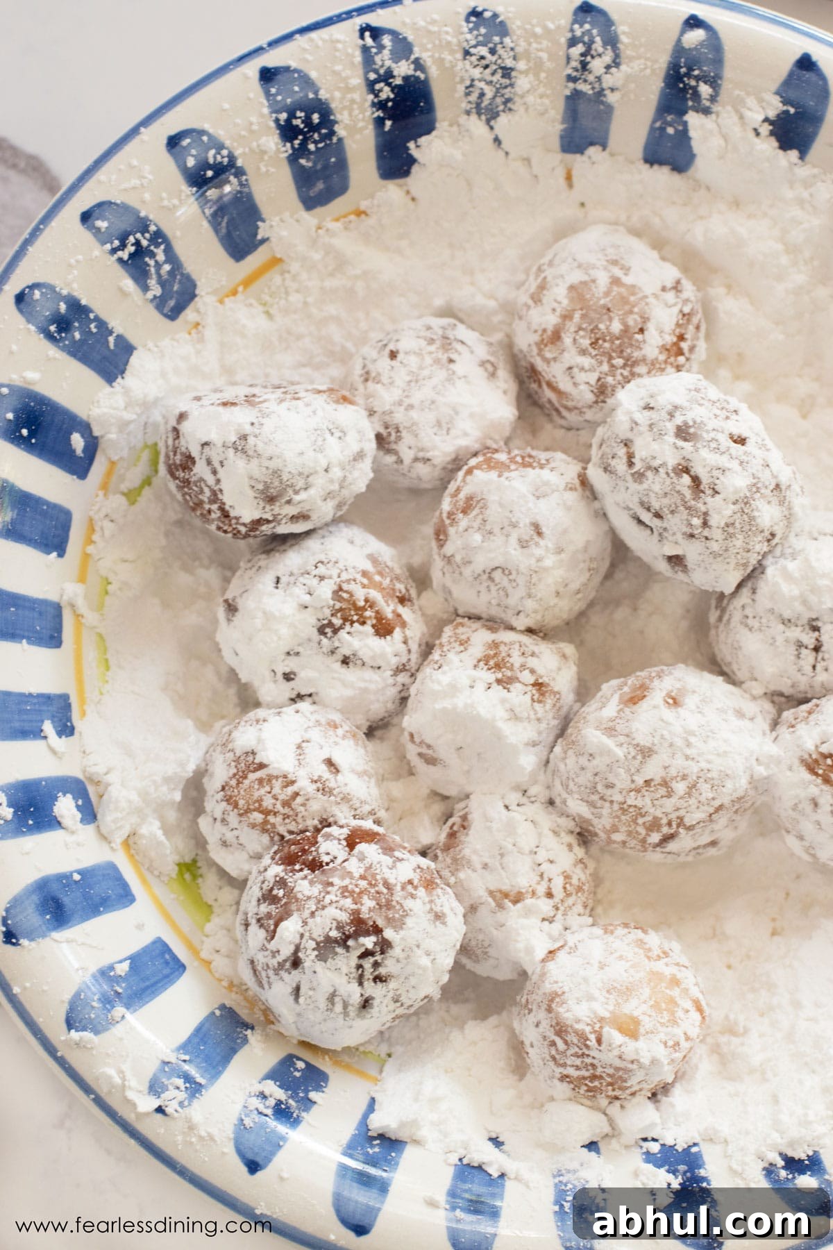 A large bowl filled with powdered sugar. Donut holes are in the sugar.