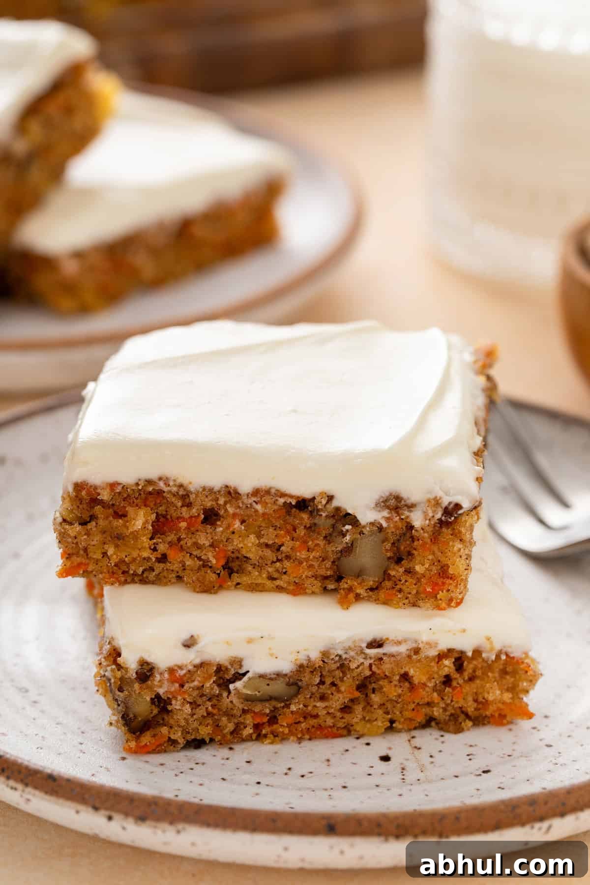 Two carrot cake bars stacked on a plate.
