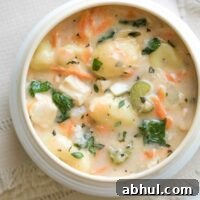 Overhead of a white bowl with creamy colored rim on cream napkin, with spoon above and fresh thyme sprigs at corner.