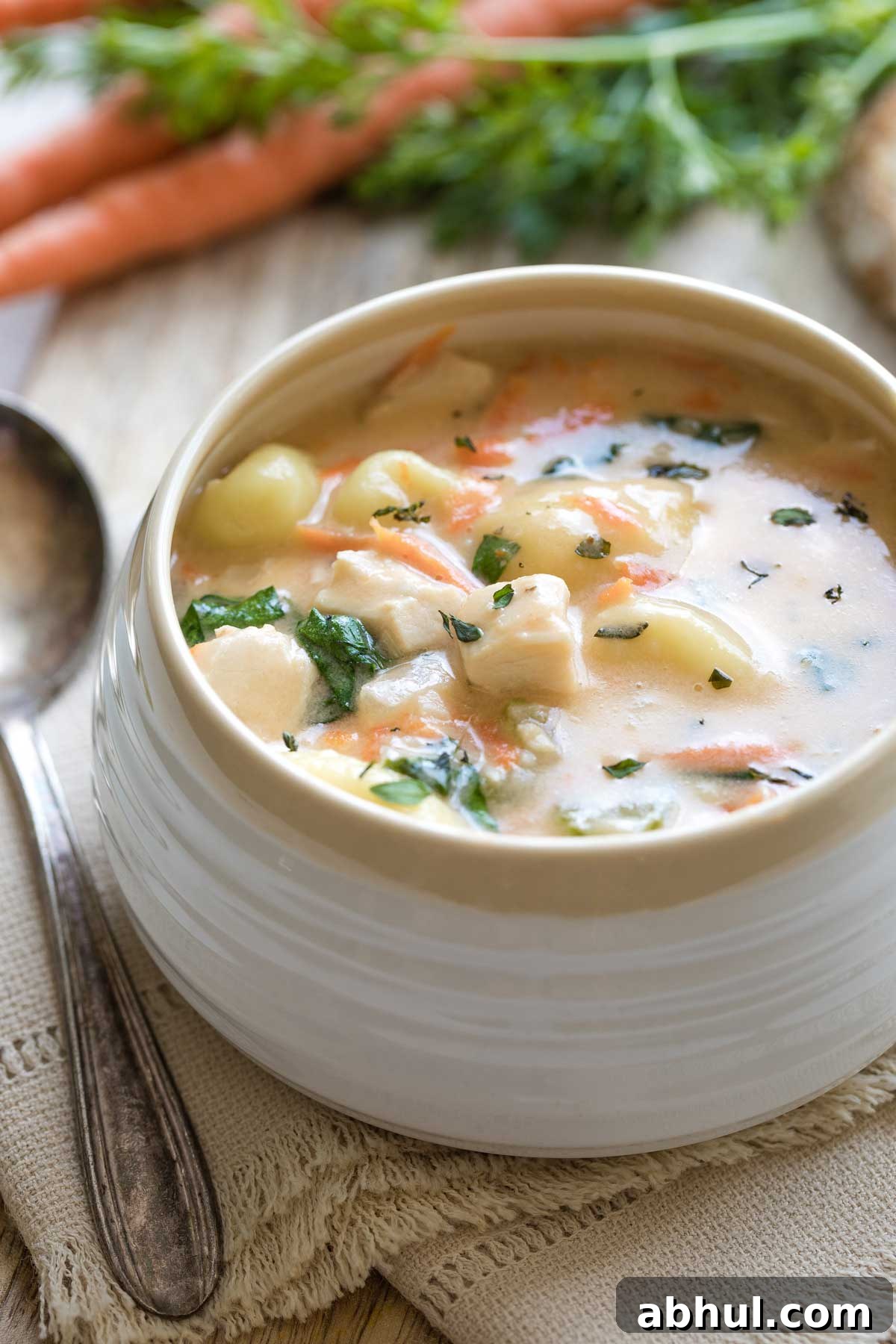 Closeup side view of one bowl of soup with fresh carrots in background and spoon at left.