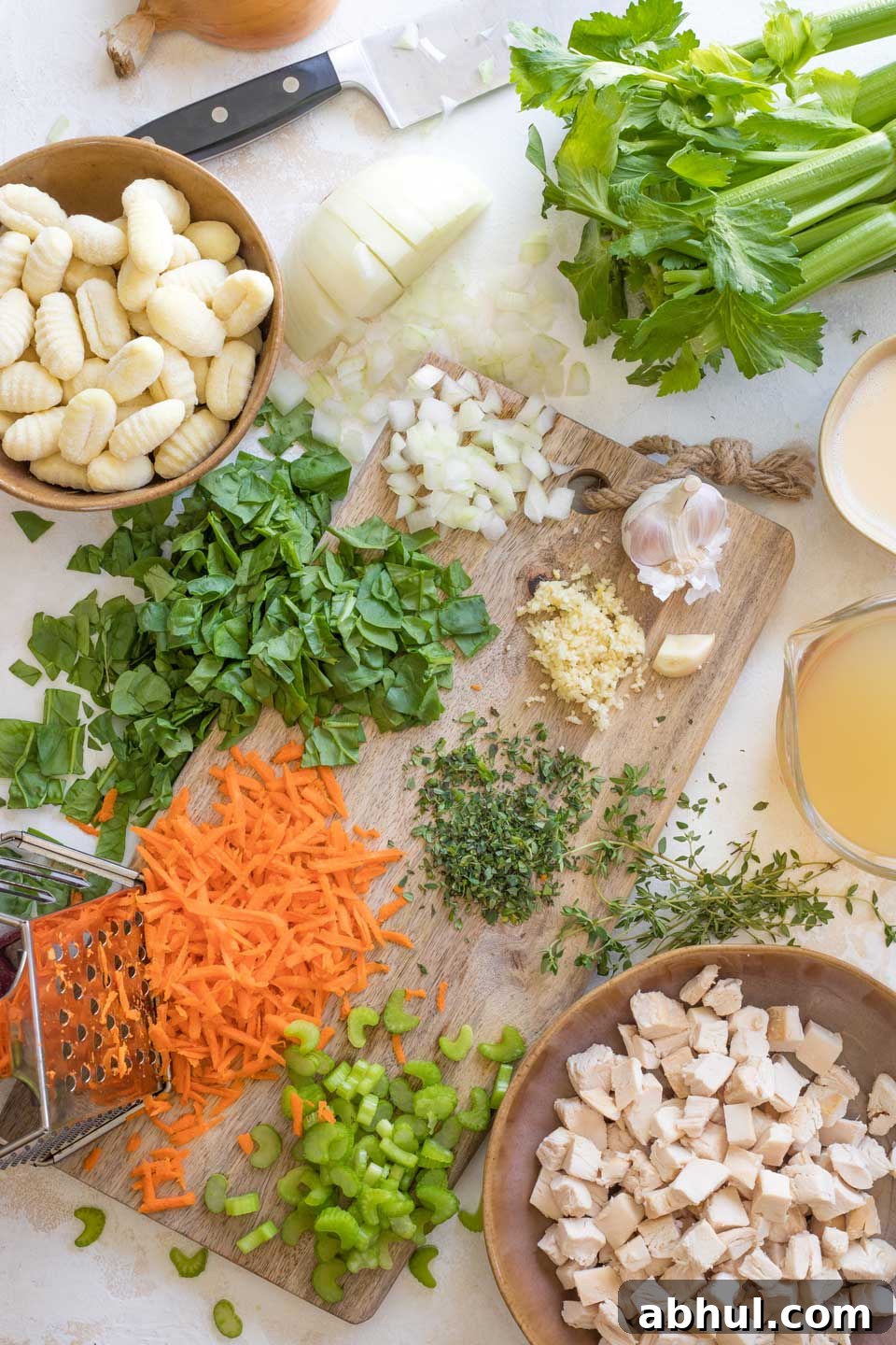 Prepped soup ingredients in bowls and little piles around cutting board, having been chopped, minced, cubed, or shredded and ready to be used.