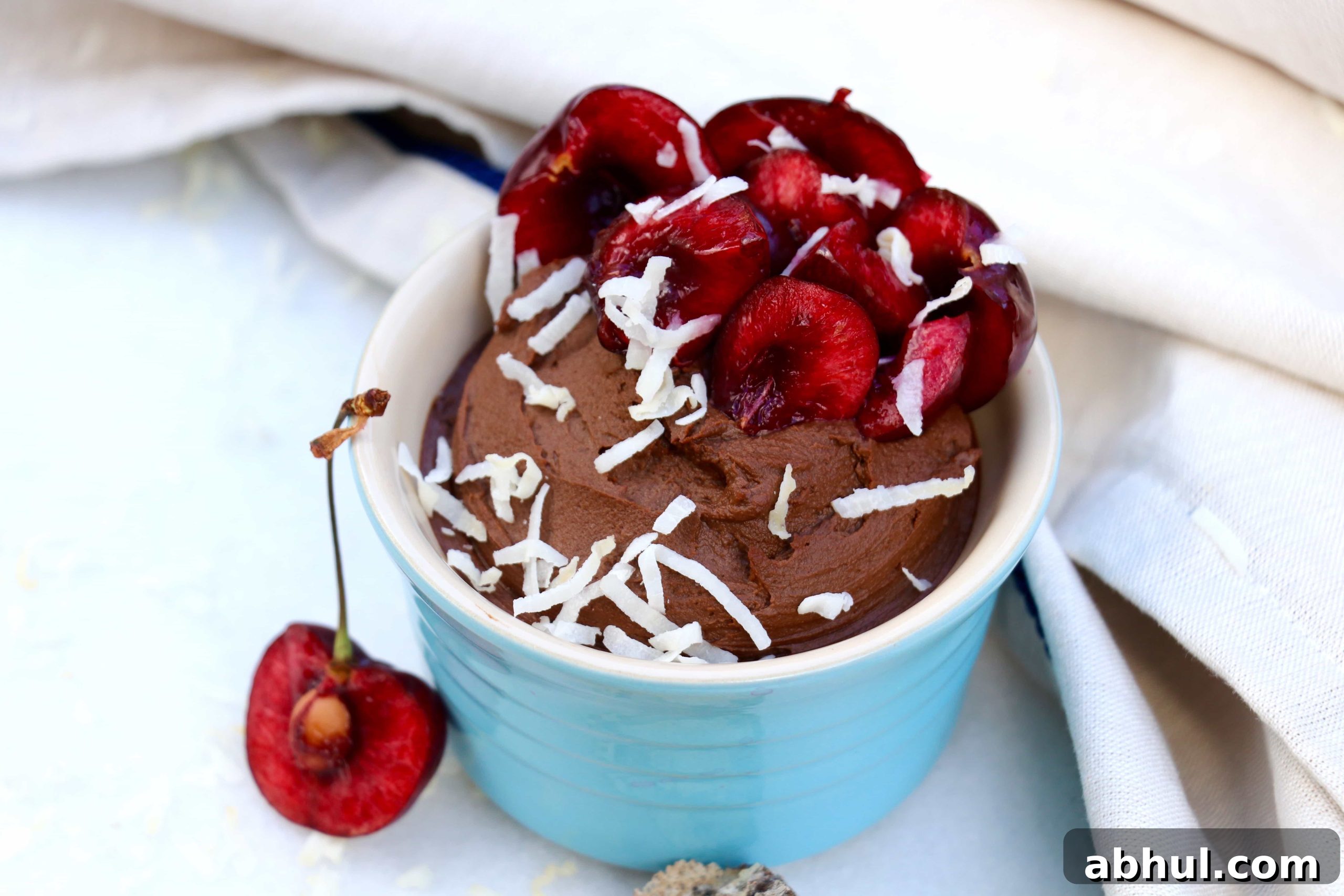 Avocado Chocolate Mousse in a light blue ramekin garnished with halved cherries and shredded coconut.